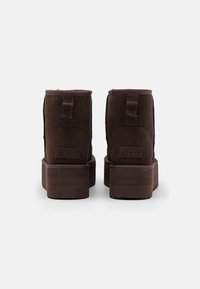 Brown suede ankle boots with a chunky platform sole, featuring a looped pull tab and tonal stitching at the sides.