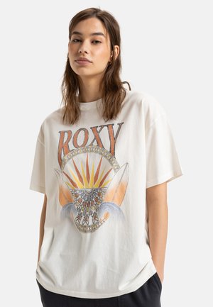 Hvid oversized bomulds t-shirt med farverig grafisk print med teksten "ROXY," solmotiv og surfbræt accenter. Løs pasform, korte ærmer.