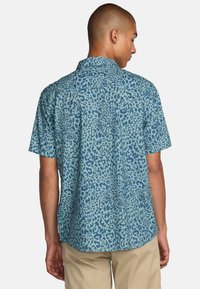 Camisa de manga corta de tejido azul con un estampado de leopardo. Cuello abotonado, ajuste relajado y detalle en la espalda.