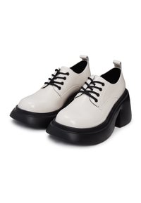 Paire de chaussures à plateforme en cuir blanc lacées avec semelles épaisses noires et talons massifs, présentées côte à côte sur fond blanc.