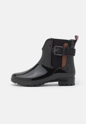 Botte de pluie noire brillante à la cheville avec panneau élastique latéral, sangle décorative à boucle, accent marron et languette avec rayure rouge et blanche.