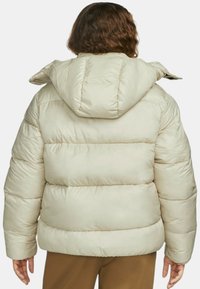 Puffer bunda v světle béžové barvě, s kapucí, prošívanou texturou a elastickými manžetami. Teplý a objemný design s zaobleným zády.