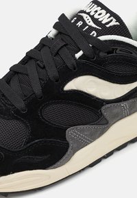 Black and gray sneaker featuring a mix of mesh and suede materials, textured accents, and a cream-colored sole. Laces are black with logo on the tongue.