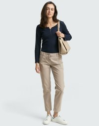 Marineblaue Langarm-Henley, hellbeige Jogginghose mit Kordelzug und weiße Sneaker; Modell hält eine beige Handtasche; einfarbiger Hintergrund.