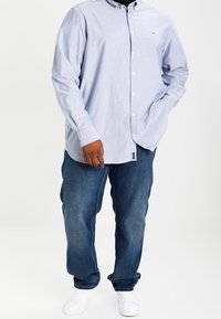 Chemise boutonnée bleu clair avec un col, associée à un jean denim bleu foncé et des baskets blanches. Tissu texturé. Coupe classique.