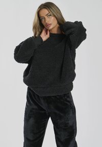 Maglione in pile nero con superficie testurizzata e soffice, colletto rotondo e polsini a coste, abbinato a pantaloni in velluto nero.