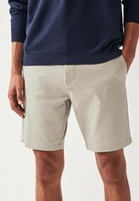 Pantalones cortos de color beige claro hechos de una mezcla de algodón, con bolsillos laterales y un diseño de frente plano, combinados con un suéter azul marino.