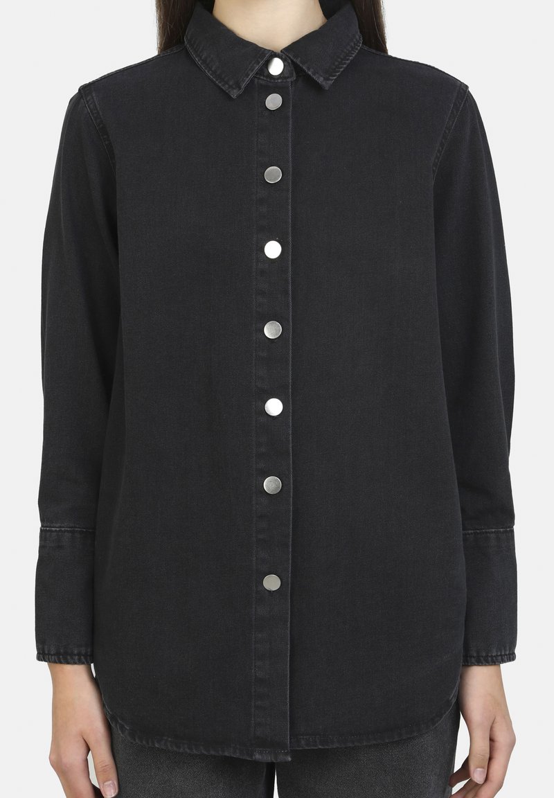 Camicia in denim nero con chiusura a bottoni, colletto a punta, maniche lunghe e bottoni in metallo argentato. Tessuto liscio con vestibilità rilassata.