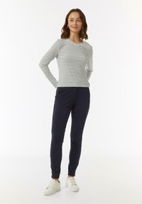 Gestreiftes Langarmoberteil in Hellgrau und Marineblau, kombiniert mit marineblauen dehnbaren Hosen und weißen Sneakers. Einfaches Design, weicher Stoff, schlanker Schnitt.