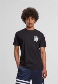 Melns kokvilnas T-krekls ar baltu grafiku, kurā ir uzraksts "UNFAIR." Klasisks piegriezums, īsas piedurknes un apaļa kakla detaļa.