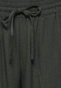 Pantalon en tissu gris foncé avec taille élastique et cordon noué devant au centre.