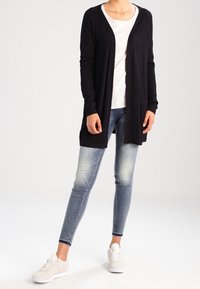 Lång, öppen front cardigan i marinblå ribbad stickning, kombinerad med en ljusgrå t-shirt, blekta skinny jeans och vita sneakers.