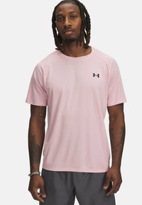 Světle růžové sportovní tričko s krátkým rukávem a kulatým výstřihem, vyrobené z texturované látky, s černým logem Under Armour na hrudi.