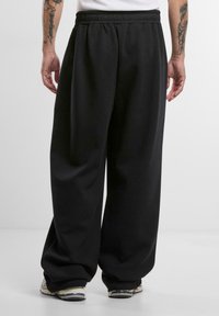 Melnas platās bikses ar elastīgu jostu, izgatavotas no mīkstas džersija auduma; piedāvā brīvu piegriezumu un maigi nokarājas.