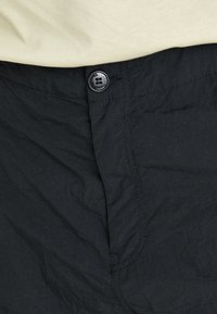 Shorts noirs en tissu texturé. Dotés de coutures visibles, d'une fermeture à bouton et d'un design ajusté avec une légère brillance.