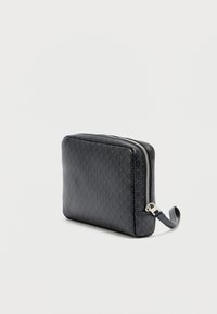 Μαύρο δερμάτινο τσαντάκι με φερμουάρ, διαθέτει γεωμετρικό σχέδιο, λεπτή ορθογώνια μορφή και πλαϊνή λαβή για εύκολη μεταφορά.