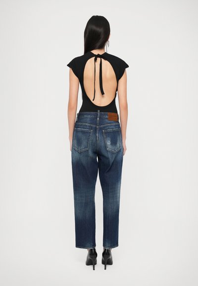 Bodysuit negro con la espalda abierta y detalle de lazo, acompañado de jeans de mezclilla azul de cintura alta, rematado con un parche de cuero y piernas ajustadas.