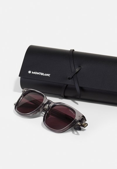 Montblanc sunglasses with gray transparent frames and dark lenses, accompanied by a black cylindrical case, secured with a black strap.