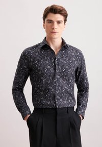 Camicia nera a maniche lunghe con un motivo paisley in grigio e bianco. Presenta un colletto classico e una chiusura con bottoni. Indossata con pantaloni neri su misura.
