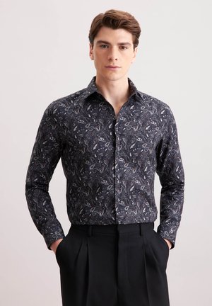 Camicia nera a maniche lunghe con un motivo paisley in grigio e bianco. Presenta un colletto classico e una chiusura con bottoni. Indossata con pantaloni neri su misura.