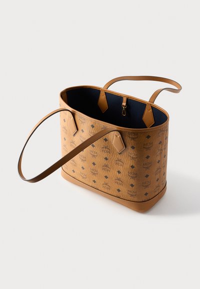 Τσάντα ώμου σε ταμπά δέρμα με υφή στην εξωτερική επιφάνεια, διαθέτει μπλε εσωτερική επένδυση, διπλές λαβές και διακοσμητικό λογότυπο με σχέδιο. Ορθογώνιο σχήμα.