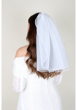 Abito da sposa in pizzo bianco con maniche a spalle scoperte; velo bianco trasparente a strati fissato con un pettine, che scorre lungo lunghi capelli castani.
