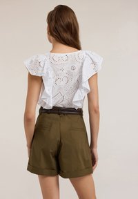 Weißes Broderie Anglaise-Oberteil mit Rüschensleeves, kombiniert mit olivgrünen, taillierten Shorts mit Gürtel und umgeschlagenen Säumen.