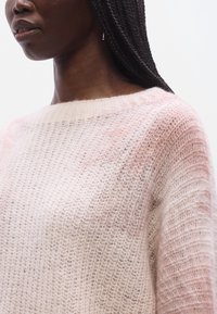 Hellrosa gestrickter Pullover mit lockerem, strukturiertem Gewebe und weitem Ausschnitt, der einen Farbverlauf mit sanften Farbtönen zeigt.