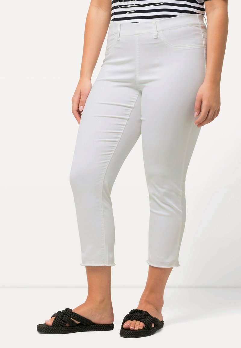 Jeans bianchi a vita alta con una trama liscia e una leggera elasticità. Vita media, tasche anteriori e orlo sfilacciato. Abbinati a sandali neri annodati.