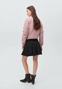 Svetlo roza oversize sweatshirt v kombinaciji s črno nabranih krilom, okroglim izrezom, teksturirano tkanino in rjavimi gležnjarji.