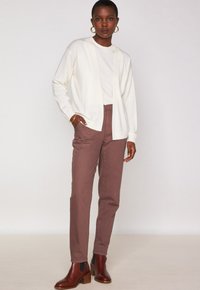 Cardigan crème sur un t-shirt blanc, associé à un pantalon marron ajusté et des bottines marron. Texture lisse, coupe décontractée, sans motifs visibles.