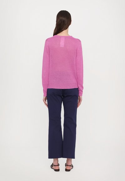Maglione rosa a maglia con maniche lunghe, scollatura rotonda e una piccola apertura sul retro, abbinato a pantaloni larghi blu navy e sandali.