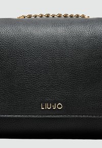 Sort struktureret lædertaske med en guld kædestrop. Har et guld "LIUJO" logo på forsiden. Kompakt rektangulær design.