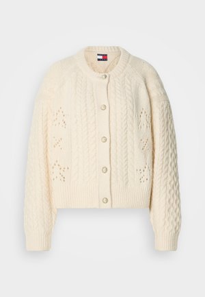 Kreemivärvi kootud kardigan, millel on nöörimustrid, nööbiga kinnitamine dekoratiivsete aktsentidega ja soonikvarrukad ning -äär. Tekstuuriga detailsus kogu toote ulatuses.