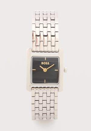 Sidabrinės spalvos metalo apyrankės laikrodis su kvadratine juoda ciferblato dalimi, auksinėmis rodyklėmis, auksiniais valandų žymekliais ir „BOSS“ logotipu 12 valandos pozicijoje.