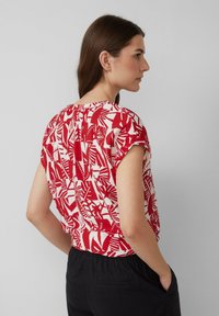 Haut à manches courtes rouge et blanc avec un motif de feuilles, décolleté rond et coupe décontractée, rentré dans un pantalon noir taille haute.