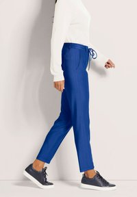 Blauwe joggingsbroek met aansnoerbare taille, zijzakken en een taps toelopend ontwerp, gecombineerd met donkere sneakers en een witte longsleeve top.