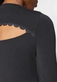 Melna garām piedurknēm tops ar viļņotu griezumu aizmugurē, izgatavots no gludas, elastīgas auduma.