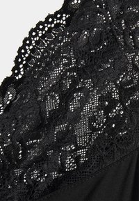 Top preto em renda com padrões e texturas intrincadas, com um tecido subjacente liso. As bordas detalhadas com padrão em escalope realçam o design.