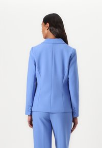 Lys blå blazer med en strukturert design, notched lapels og tre-knapps mansjetter. Har skreddersydde sømmer for en tettsittende silhuett.