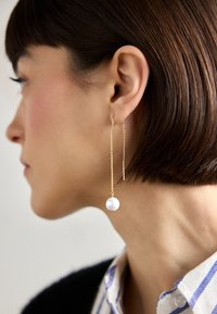 Gouden kettingoorbellen met een grote, ronde, witte parel als hanger, voorzien van een strak ontwerp en delicate kettingdetails.