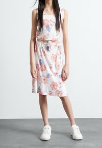Sukienka w kwiatowy wzór z białym tłem i różowo-niebieskimi kwiatami, z paskiem wiązanym na supeł i luźnym krojem. Połączona z białymi trampkami.