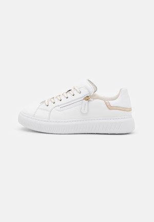 Hvid lavtop sneaker med snørebånd og sidelukning med lynlås, beige accenter og en tyk, tekstureret sål på en ensfarvet baggrund.