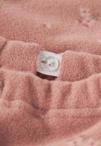 Mäkká ružová fleece textília s textúrovaným povrchom, s bielym elastickým pásom a detailom priehľadného gombíka na zapínanie.