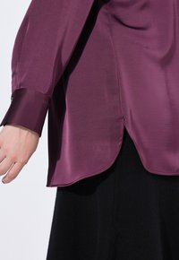 Lässiges, langärmeliges Hemd aus tiefpurpurfarbenem Satin mit abgerundetem Saum. Verfügt über Ärmelmanschetten und eine glatte, glänzende Textur.
