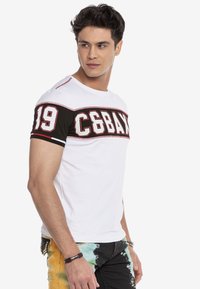 Witte t-shirt met korte mouwen en zwarte accenten, met bold rode tekst "C6BAX 19" op de borst. Glad stof, casual pasvorm, ronde halslijn.