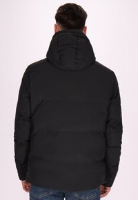 Giacca a vento nera con cappuccio rimovibile, mostrata di spalle. Caratterizzata da una texture liscia e un design imbottito, con una vestibilità comoda.
