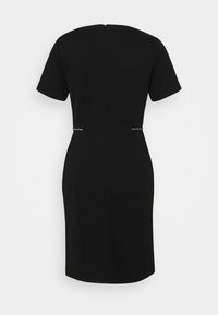 Robe noire longueur genou avec manches courtes, taille cintrée et détail de fermeture éclair visible dans le dos sur fond uni.
