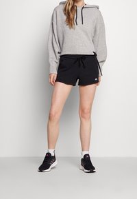 Grå hoodie med snoddar, i kombination med svarta shorts med elastisk midja. Svarta sportskor med rosa detaljer. Vita strumpor.