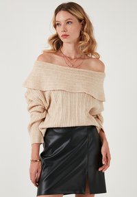Bežna off-shoulder pulover s rebrasto teksturo in širokim ovratnikom, v kombinaciji s črno usnjeno krilo z sprednjim razporkom.